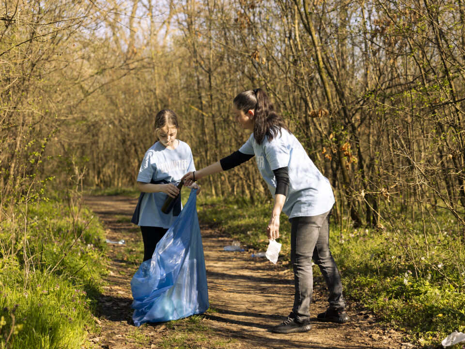 Na fotografiji ženska in deklica v gozdu pobirata smeti.